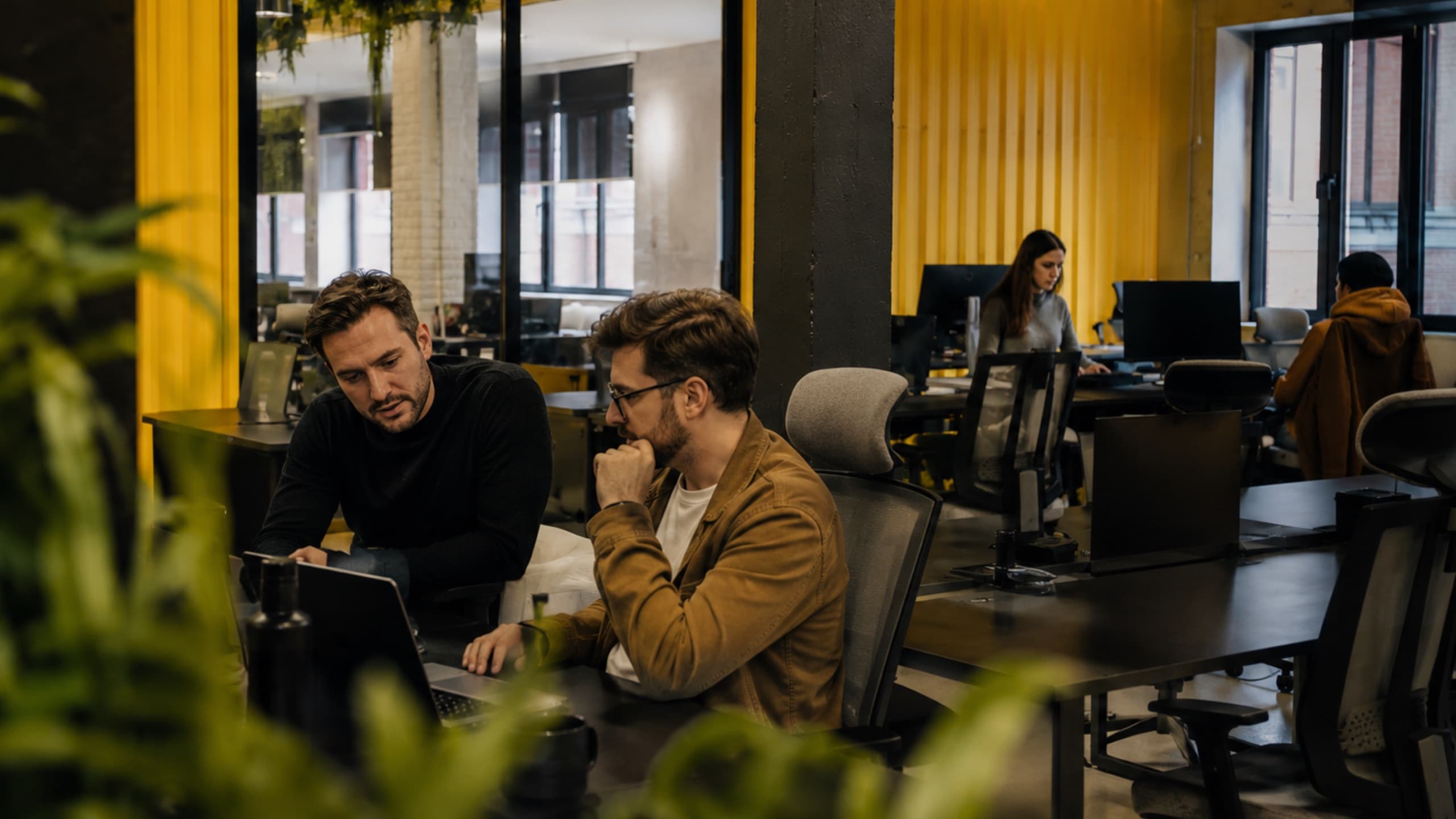 Two members working out the week's announcement over a laptop on the tershouse coworking floor